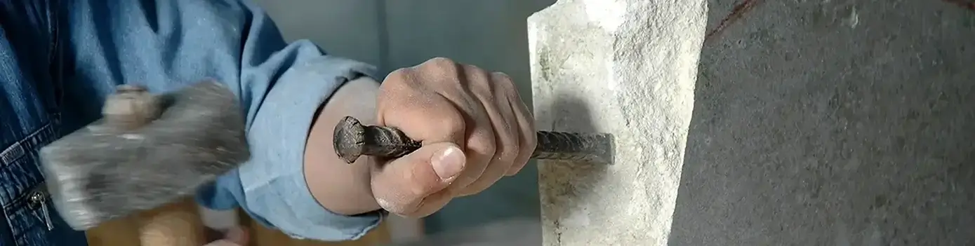 Ein Steinmetz bearbeitet einen weißen Marmorstein mit Hammer und Meisel