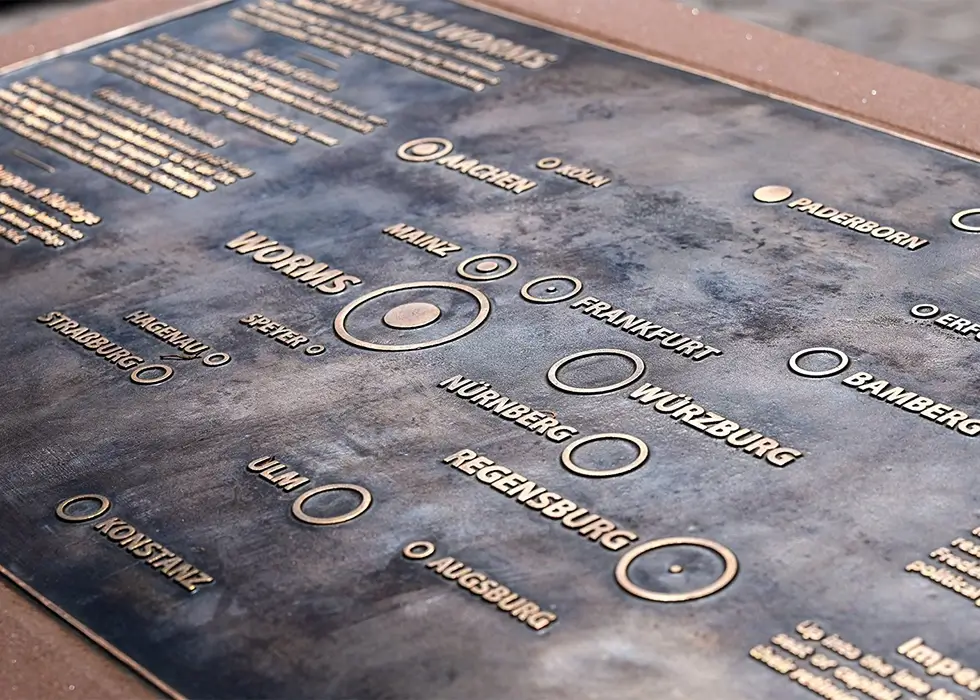 Eine große Messingsplatte steht auf dem Marktplatz, mit vielen Städte eingefasst